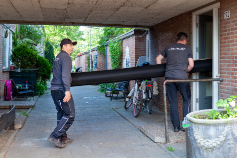 Twee mannen van ed Buurtservice brengen rol tapijt binnen in een woning