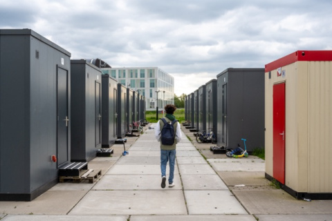 Bewoner met rugzak loopt tussen de woonunits van noodopvanglocatie