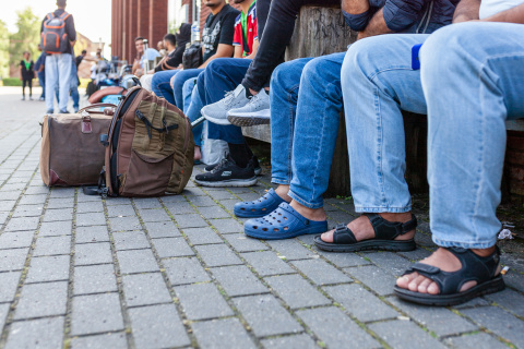 Op een lange rij zie je de benen en bagage van wachtenden in Ter Apel