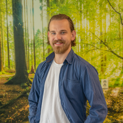 Man met baard staat voor muur met behang van een bos